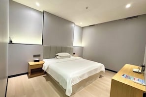 Ein modernes Hotelzimmer mit einem großen Bett, Nachttischen, einem Schreibtisch mit Stuhl und einem wandmontierten Fernseher.
