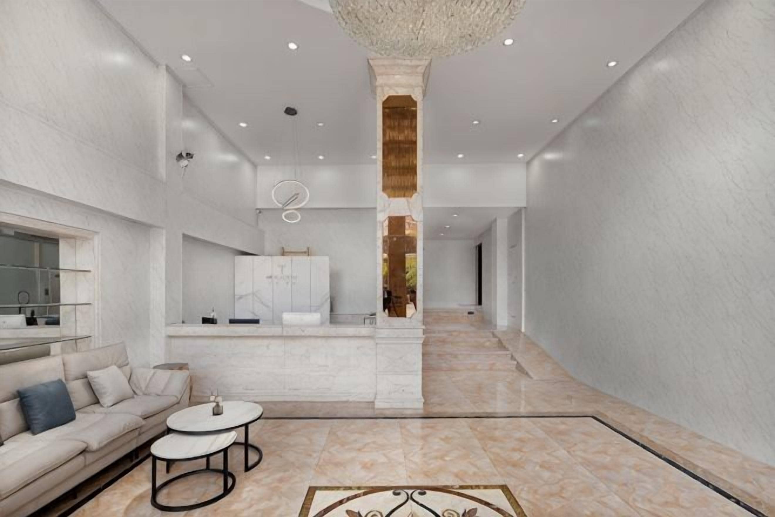 Un hall de hotel espacioso con una columna central, un sofá, una mesa de centro y una zona de cocina al fondo.