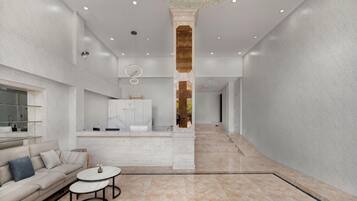 Un hall de hotel espacioso con una columna central, un sofá, una mesa de centro y una zona de cocina al fondo.