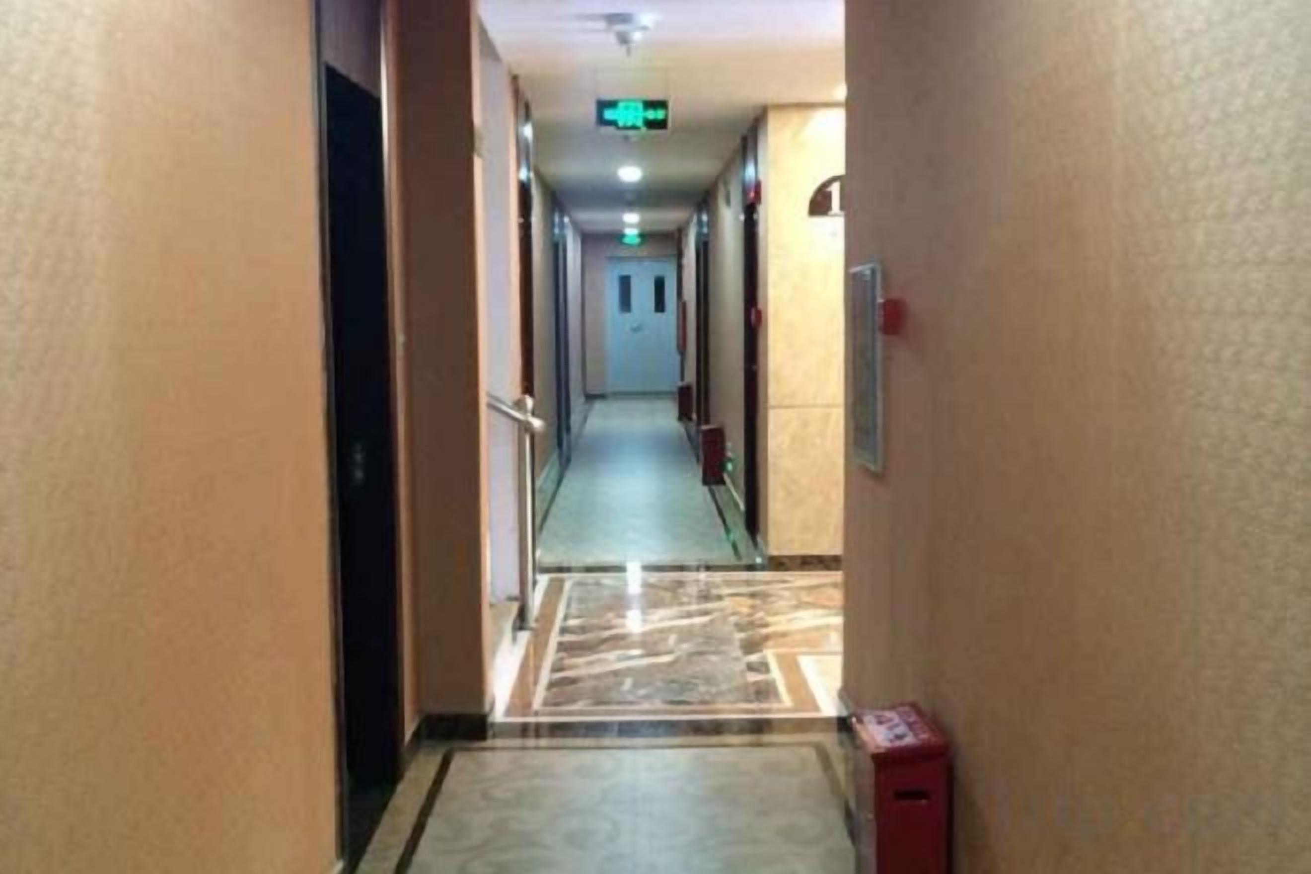 A hotel corridor with a marble floor, doors on both sides, and a fire alarm on the right.