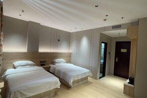 Una habitación de hotel moderna con dos camas individuales, un cabecero de madera, una mesita de noche pequeña y una puerta oscura.