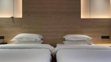 Habitación de hotel con dos camas, cabecero de madera y mesitas de noche fijadas a la pared.