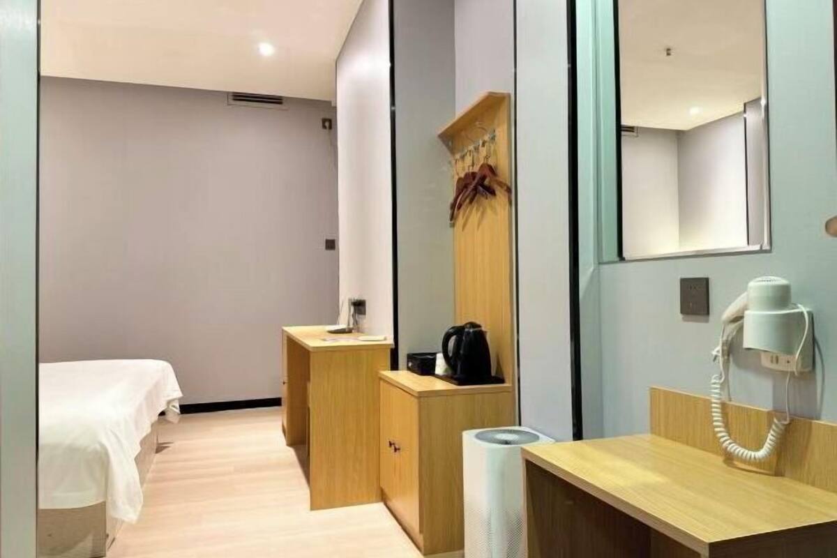 A hotel room with a bed, a wooden desk, a mirror, a telephone, and a radiator.