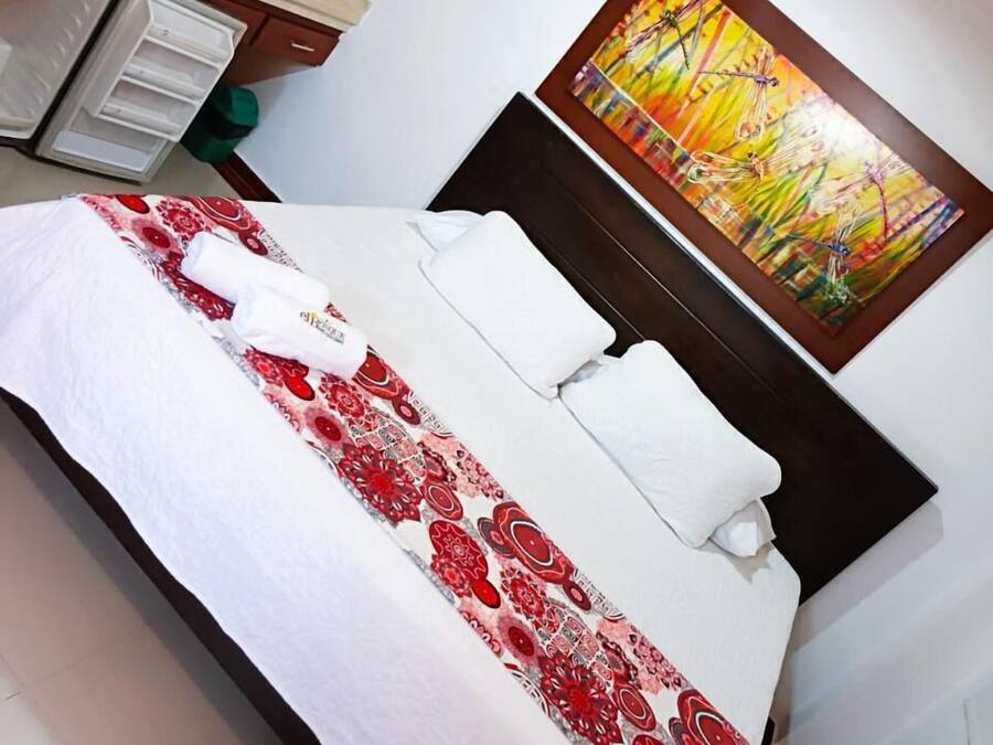 A hotel room with a bed, a painting on the wall, and a television on a stand.