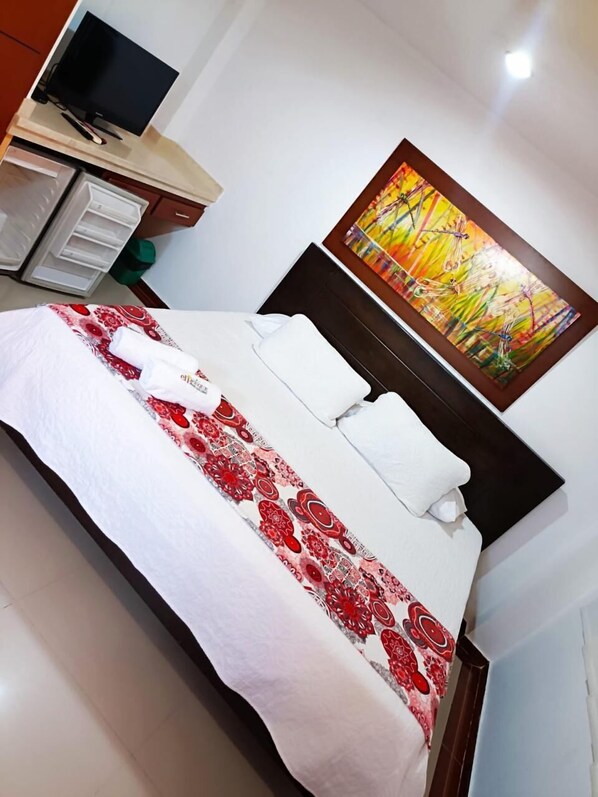 Une chambre d’hôtel avec un lit, un tableau accroché au mur et un téléviseur posé sur un meuble.