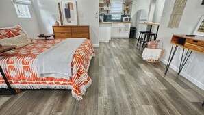 Une chambre moderne avec un grand lit, un plancher en bois et, au fond, un coin cuisine.