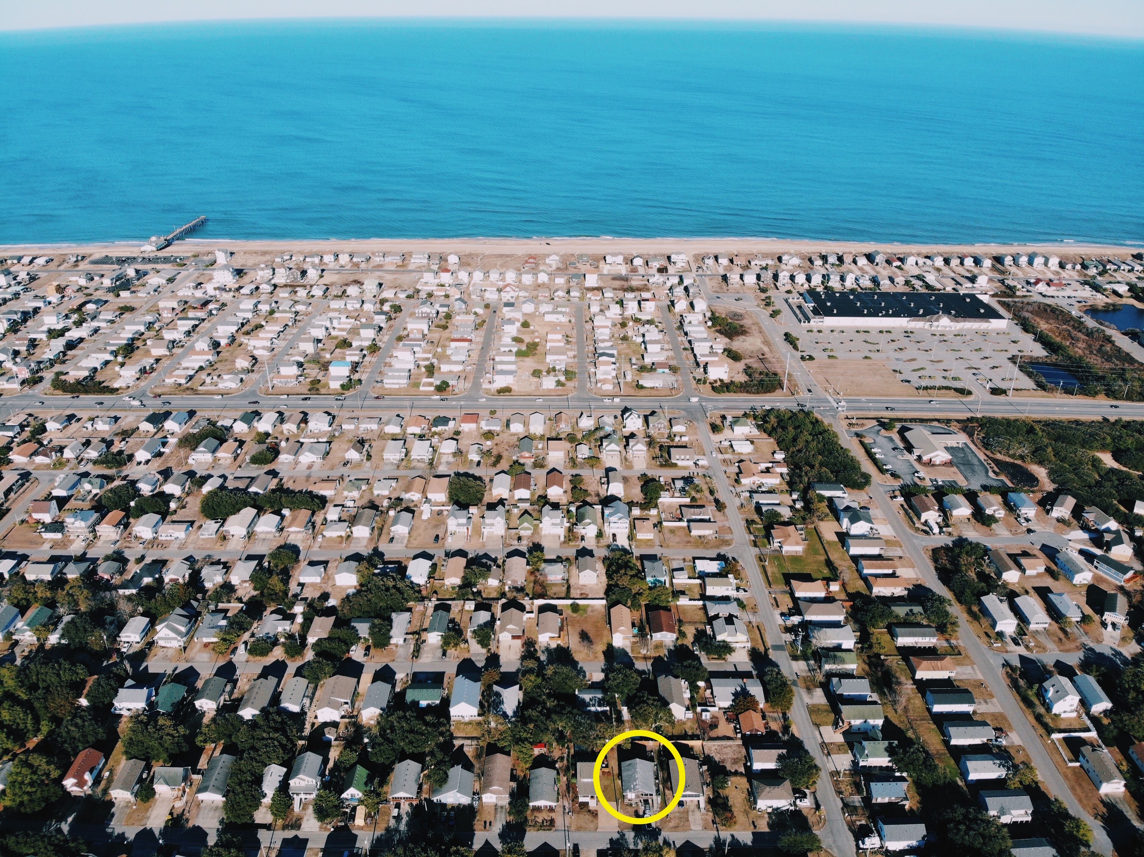 Vista aérea de una zona residencial costera con numerosas casas, un puerto deportivo y una carretera que conduce a la playa.