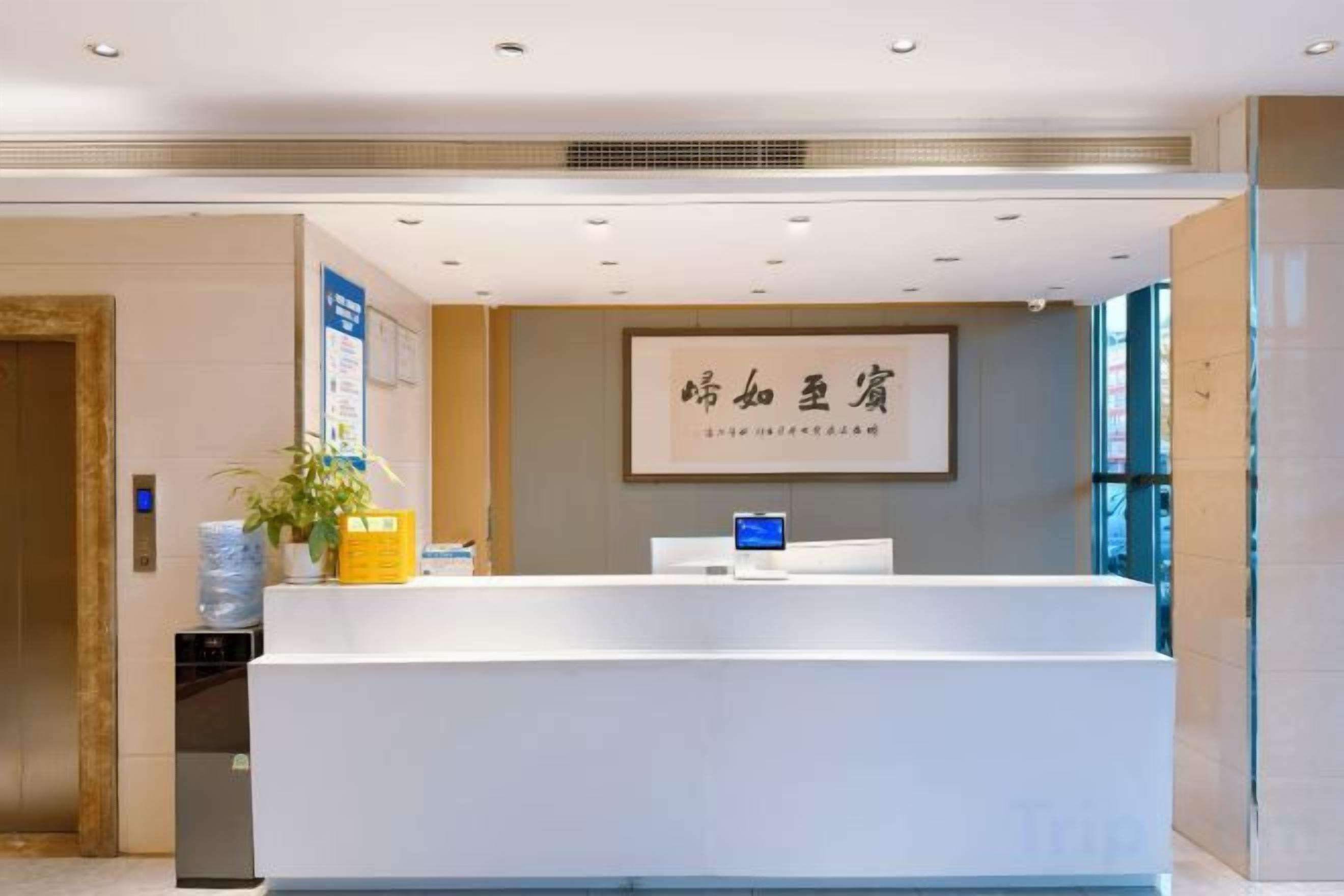 A reception desk with a framed sign, a potted plant, and a blue information board.