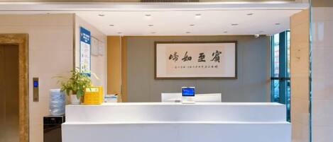 A reception desk with a framed sign, a potted plant, and a blue information board.