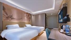 Habitación de hotel con dos camas, un escritorio, una silla, un televisor y una pared decorada con obras de arte.