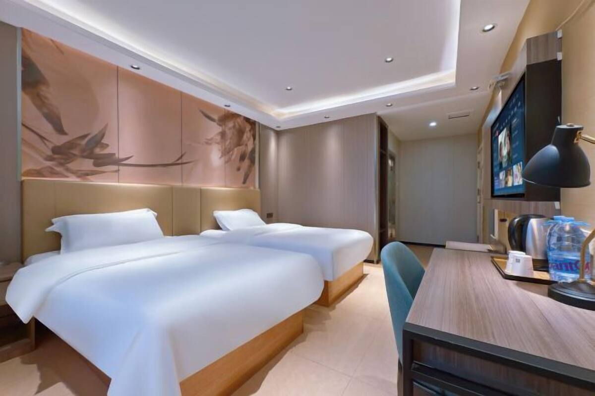 A hotel room with two beds, a desk, a chair, a TV, and a wall with artwork.