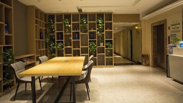 Un moderno vestíbulo de hotel con un mostrador de recepción de madera, una larga barra de recepción y un área de estar con mesa y sillas de madera.