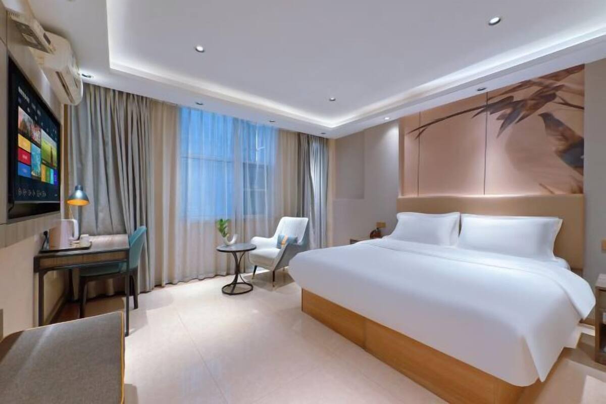 A modern hotel room with a large bed, a desk with a chair, a small table, and a TV on the wall.