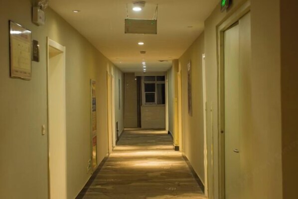 A long, narrow hallway with doors on both sides, recessed lighting on the ceiling, and a tiled floor.