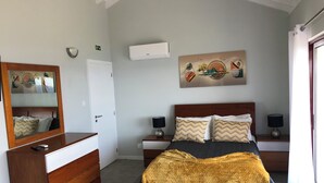 Een slaapkamer met een bed, nachtkastjes, een dressoir, een spiegel, een airconditioner en een schilderij aan de muur.