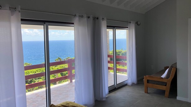 Een kamer met een grote schuifglazen deur die uitkomt op een balkon met uitzicht op de oceaan.