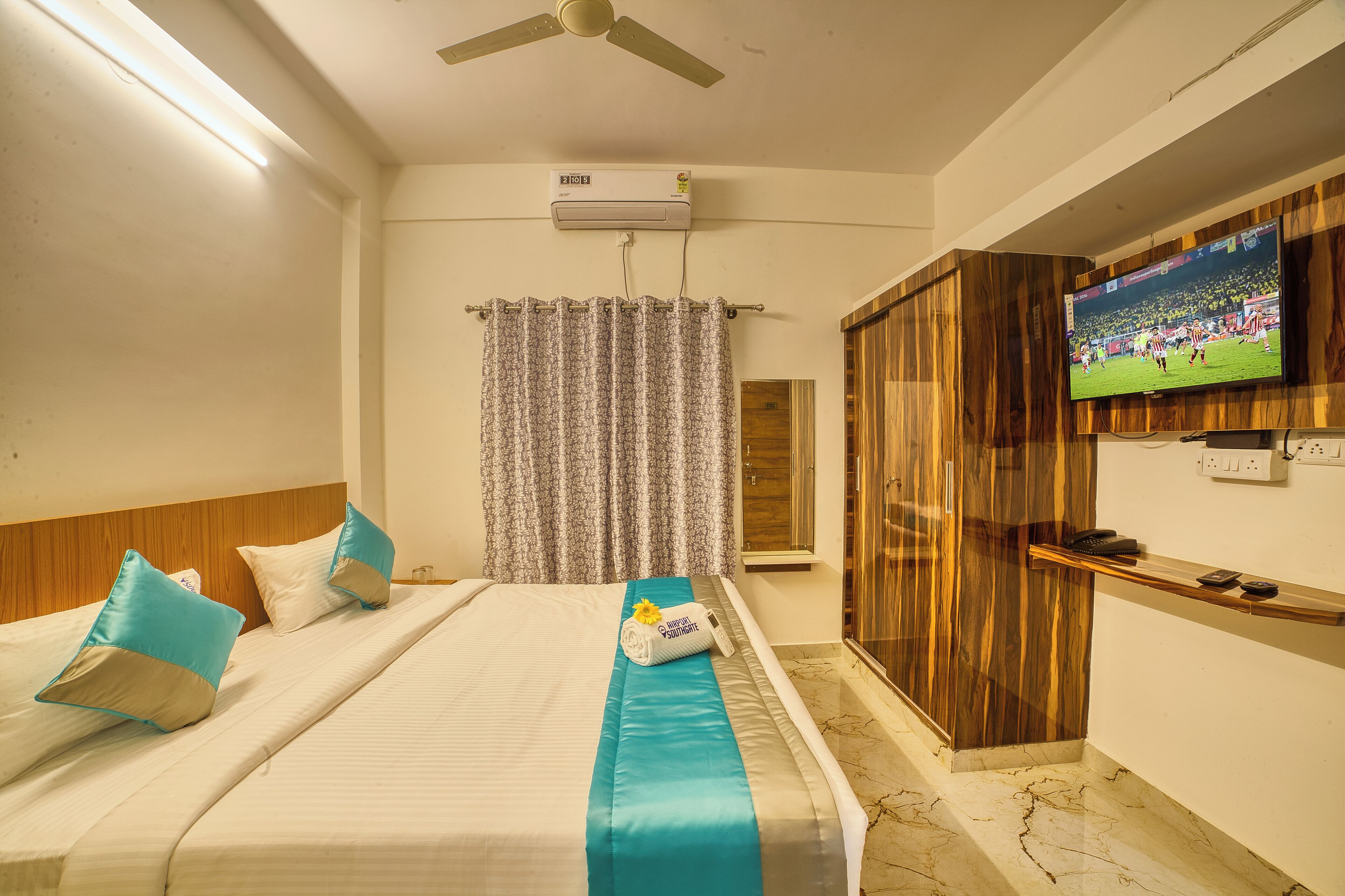 A hotel room with a bed, a TV mounted on the wall, a ceiling fan, and an air conditioning unit.