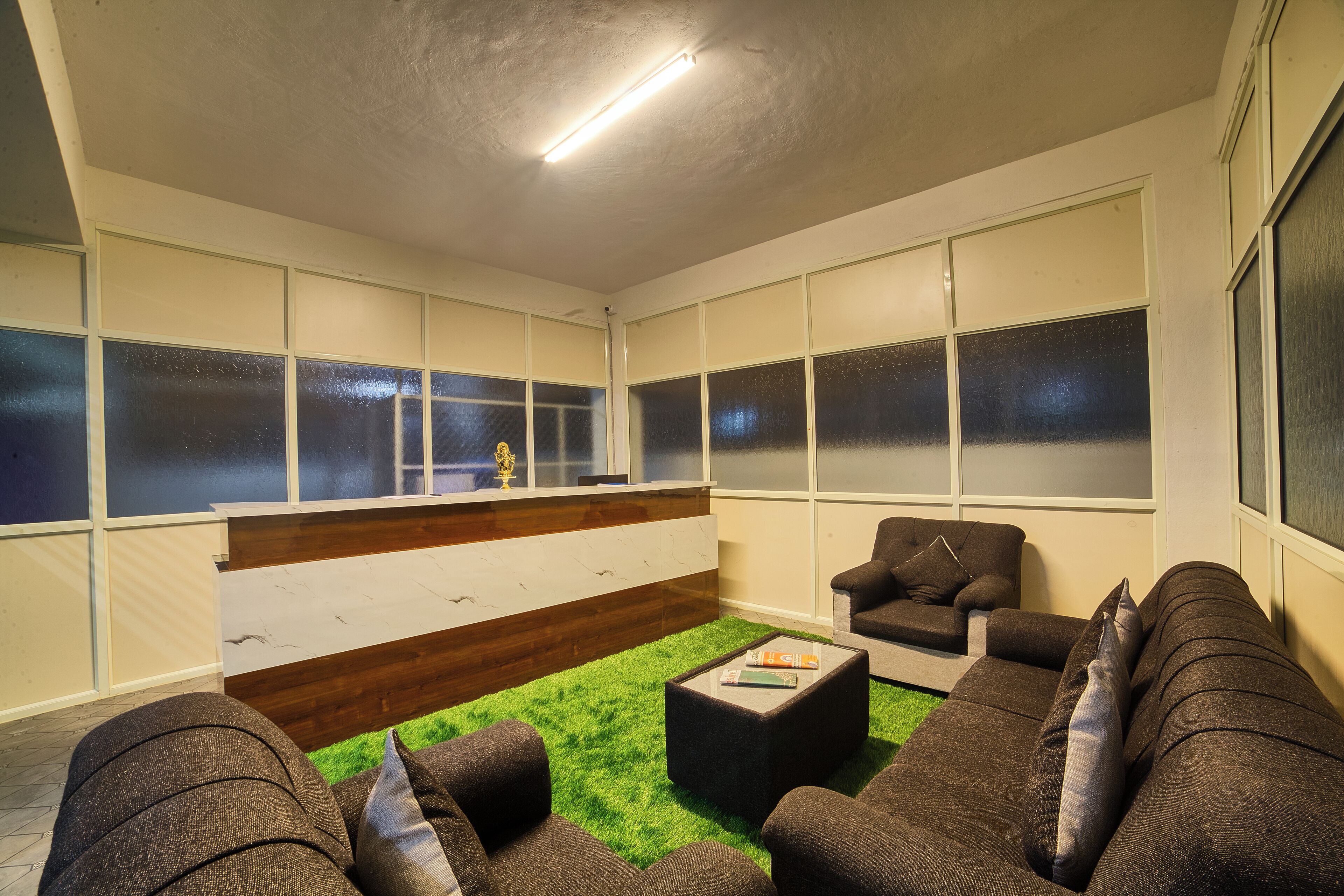 A modern lounge area with a green carpet, dark sofas, and a reception desk.