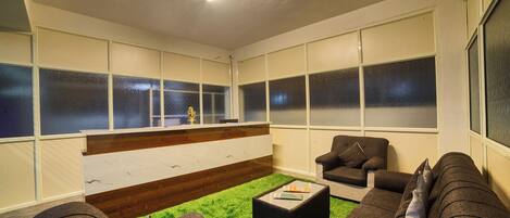 A modern lounge area with a green carpet, dark sofas, and a reception desk.