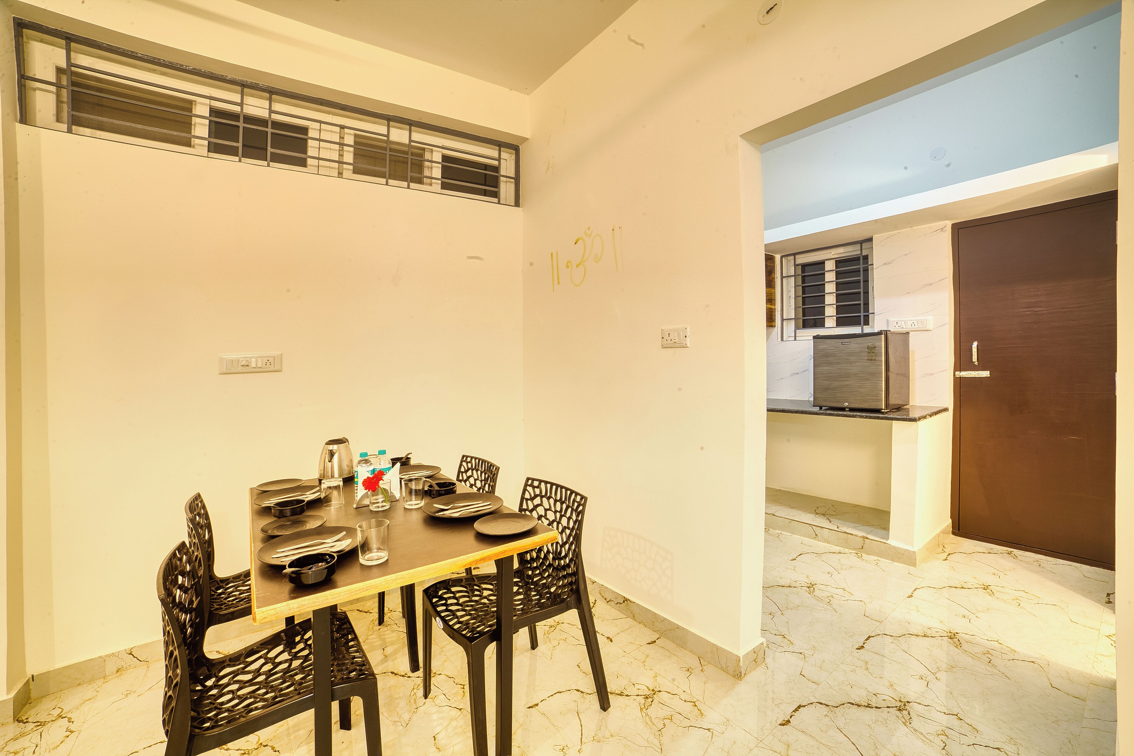 A dining area with a marble floor, a wooden table set with plates, glasses, and cutlery, and black chairs.