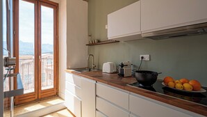 Une cuisine avec un plan de travail en bois, des placards blancs, un évier, une cuisinière et une vue sur les montagnes, visible à travers une porte coulissante.