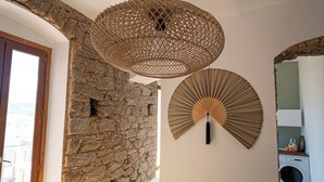 Une pièce avec un mur en pierre, un luminaire suspendu au plafond fait de fibres tressées et un ventilateur fixé au mur.