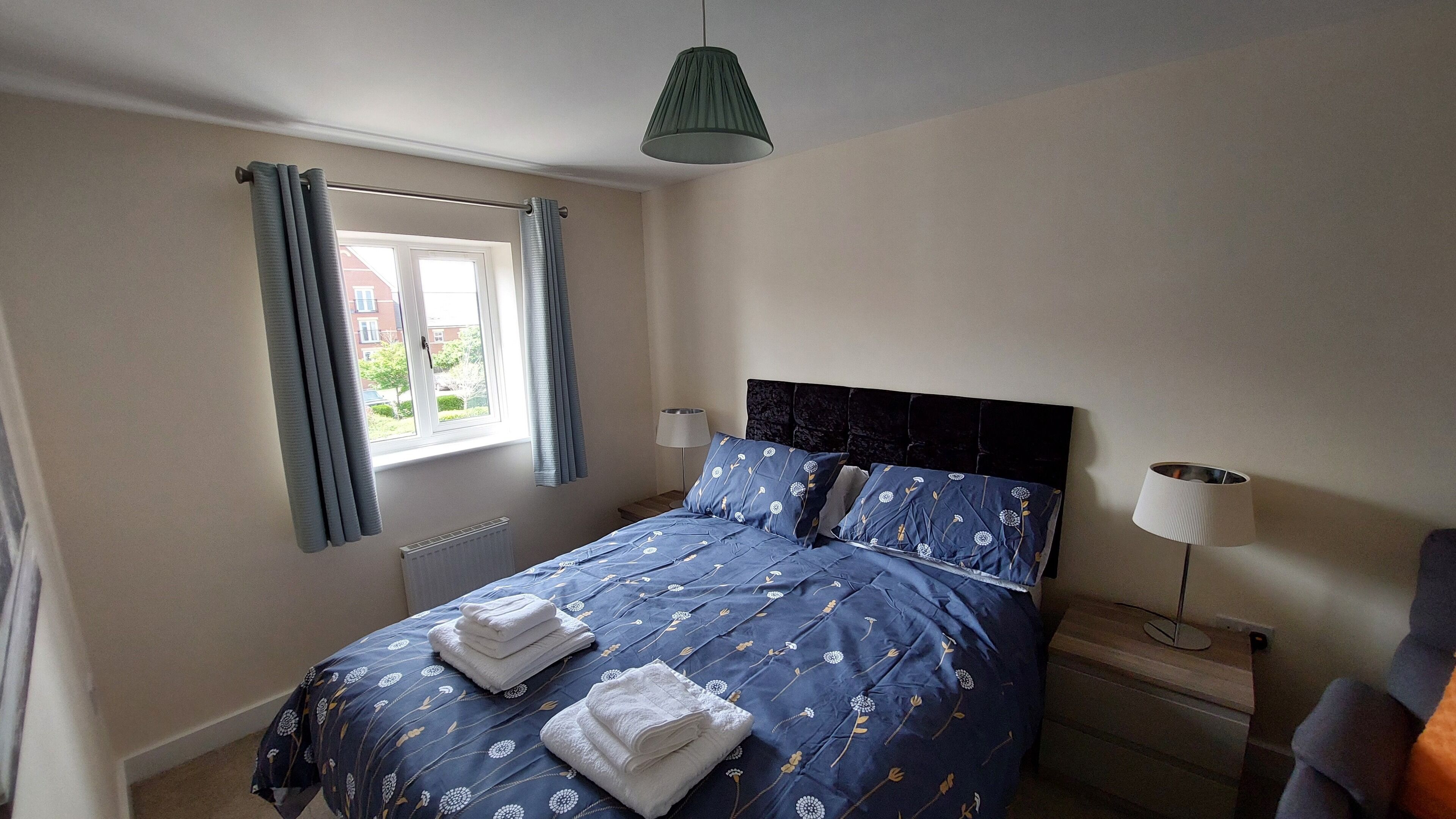 Un dormitorio con cama, ventana con cortinas, radiador, lámpara de mesita de noche y lámpara de pie.