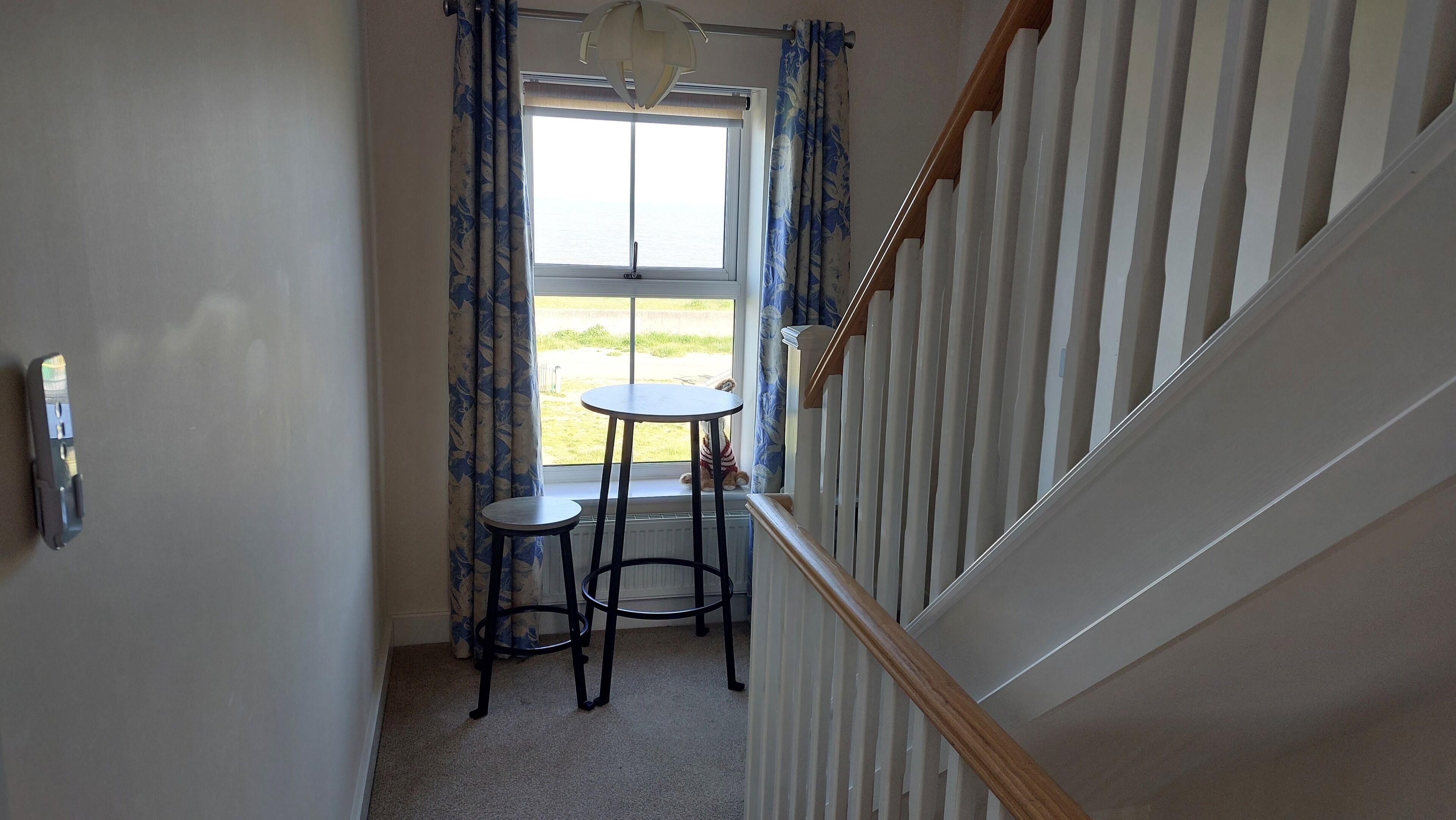 A narrow hallway with a window, a small round table, and a chair.