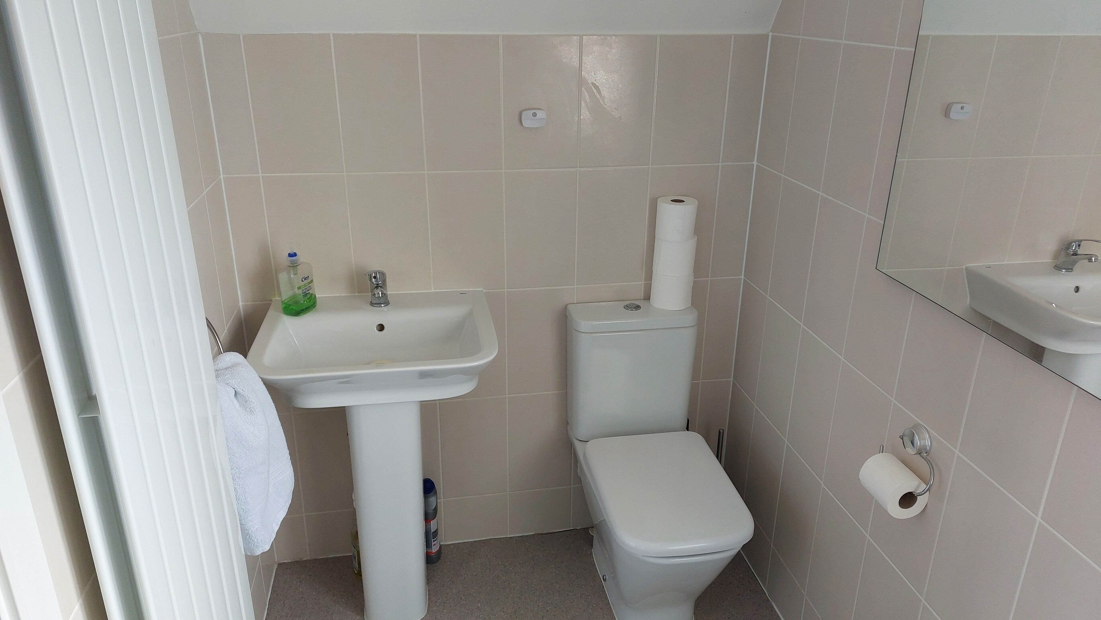 A bathroom with a white sink, toilet, and bidet. There is a towel hanging on the wall and a bottle of liquid soap on the sink.