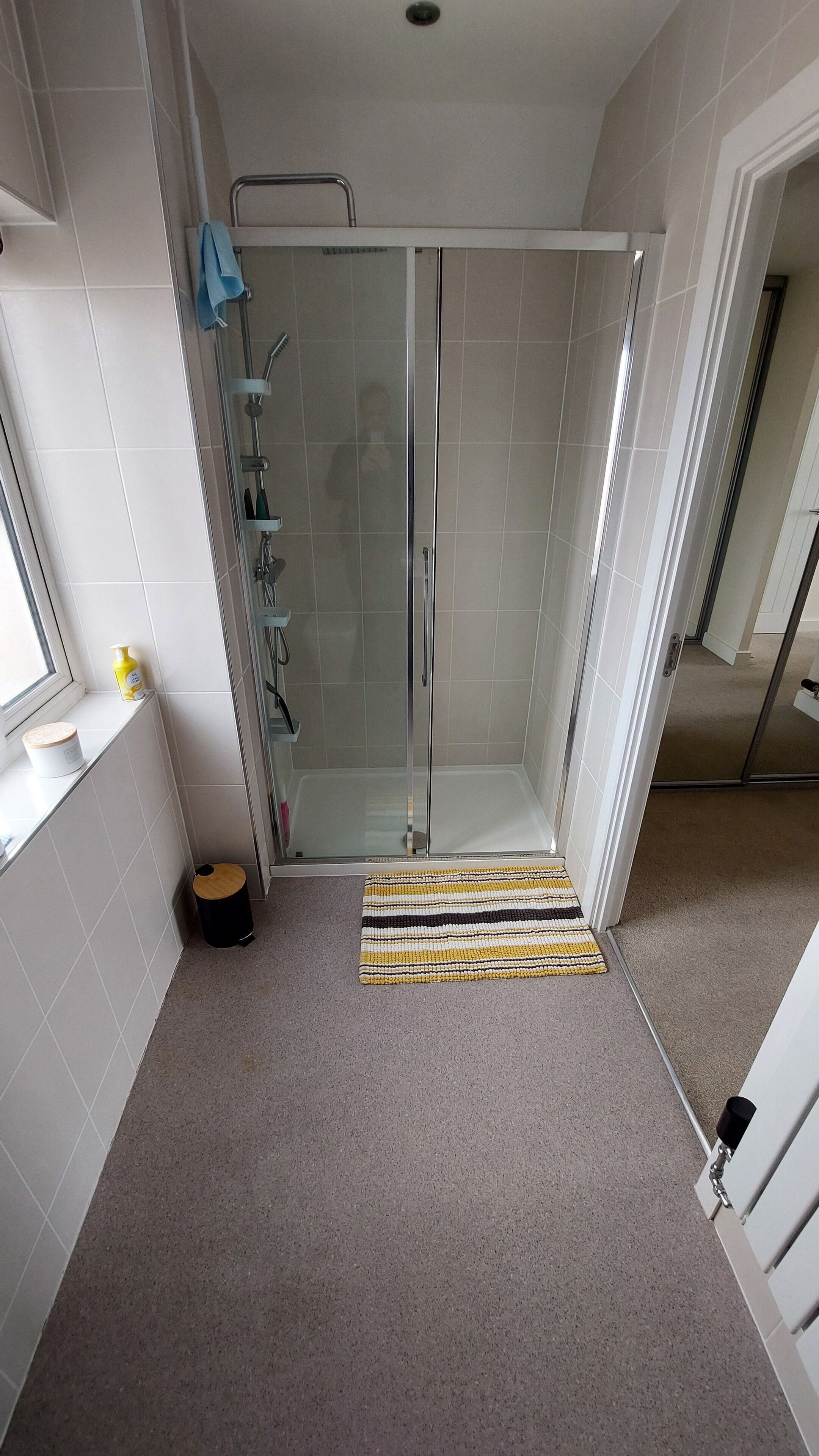 Un baño moderno con ducha de vidrio, paredes de azulejos blancos y una pequeña ventana.