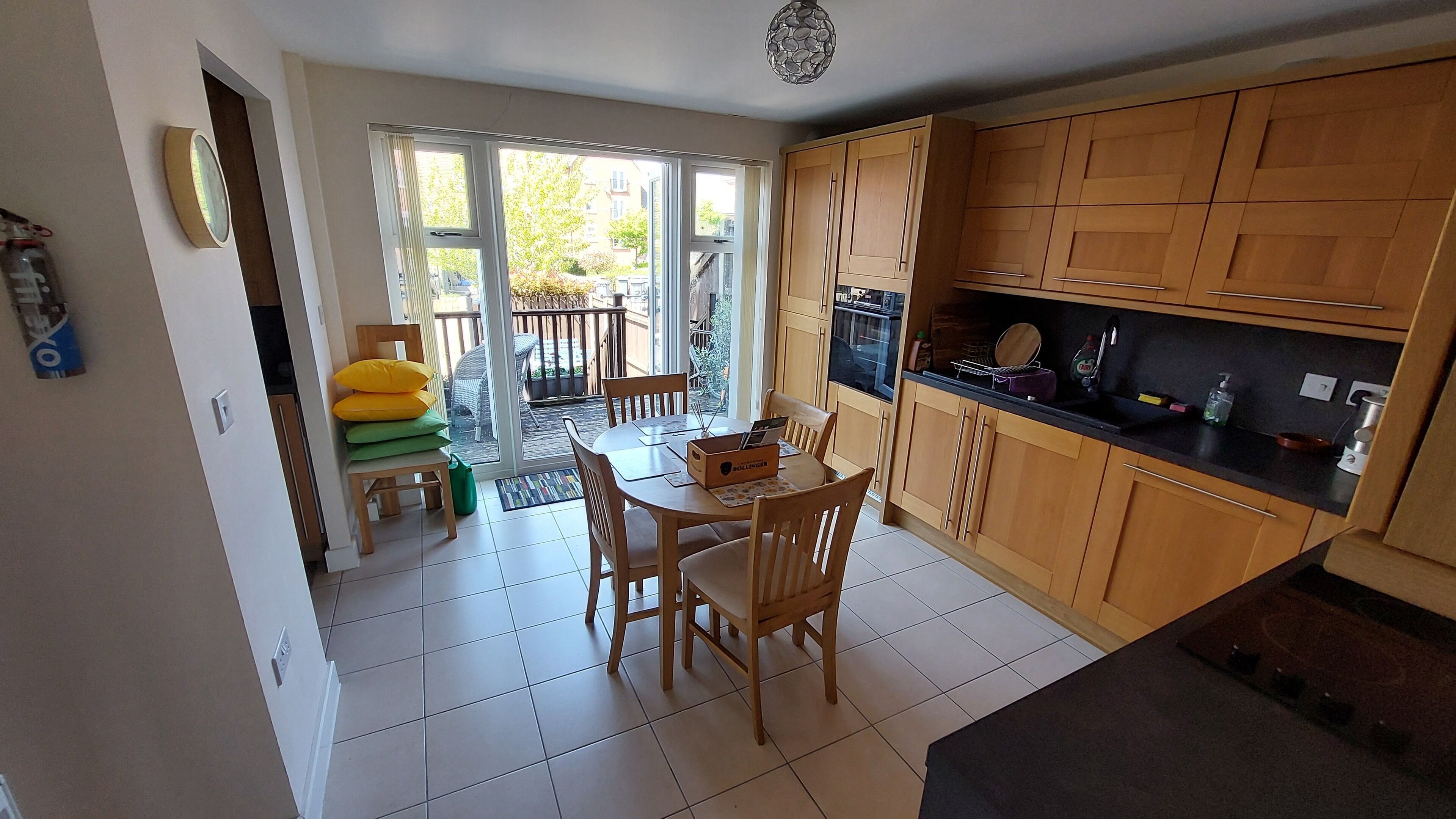 Une cuisine avec des meubles de rangement en bois, une table à manger avec des chaises et une fenêtre donnant sur un jardin.