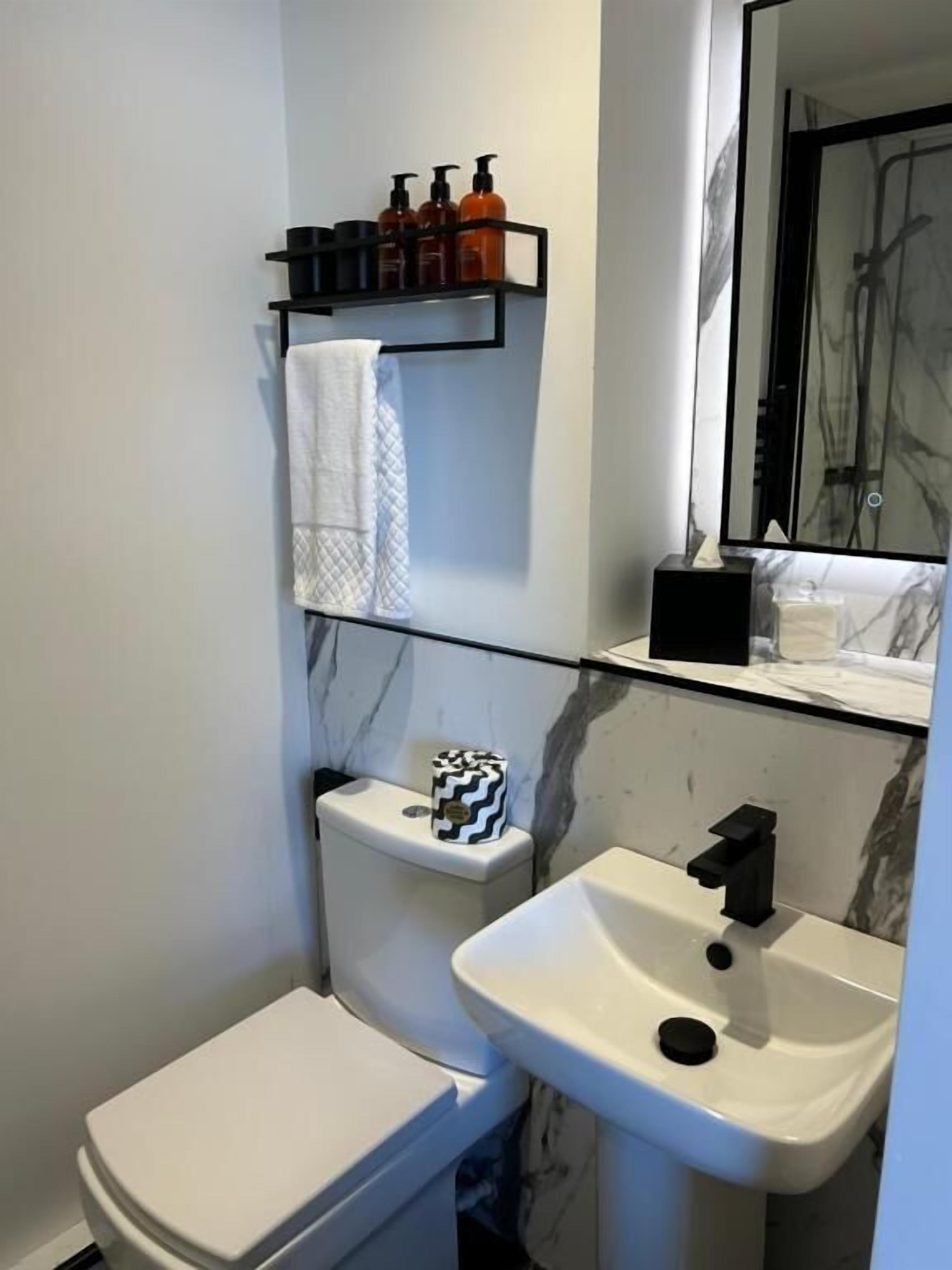 Baño pequeño con inodoro, lavabo y estante con artículos de aseo.
