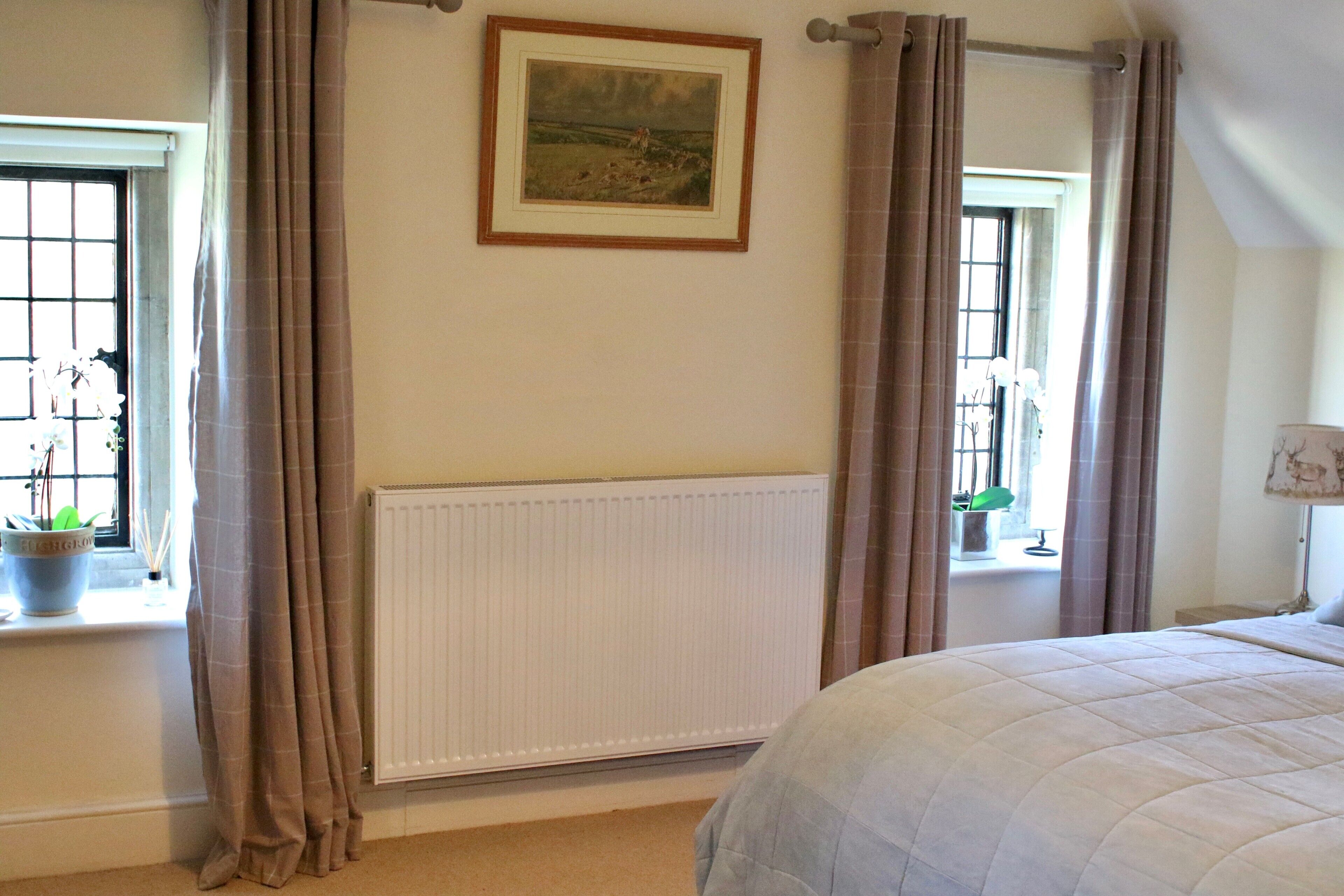 A bedroom with a large bed, a radiator, and curtains on the windows.