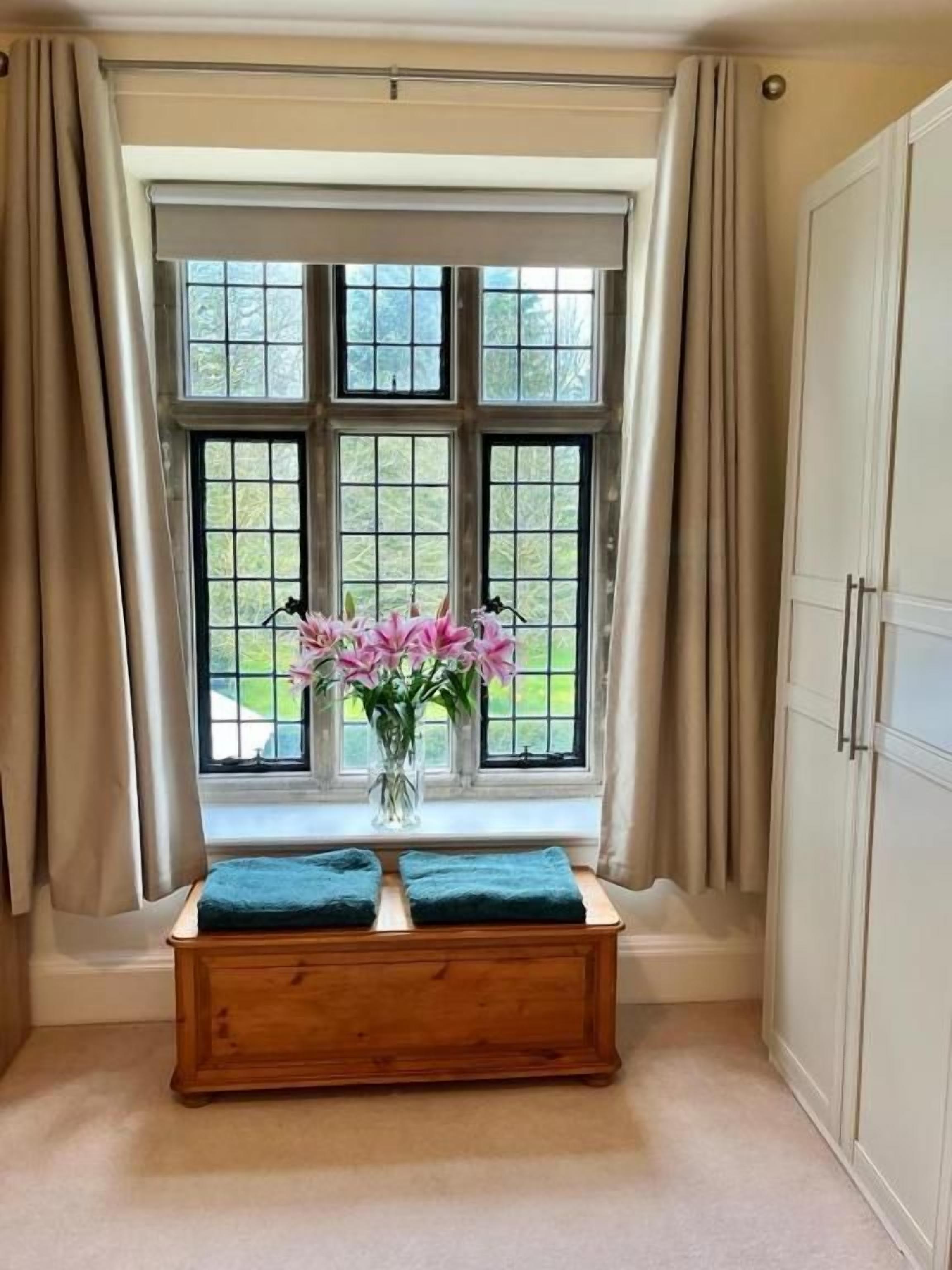 A room with a window, a wooden bench, a vase with flowers, and a wardrobe.