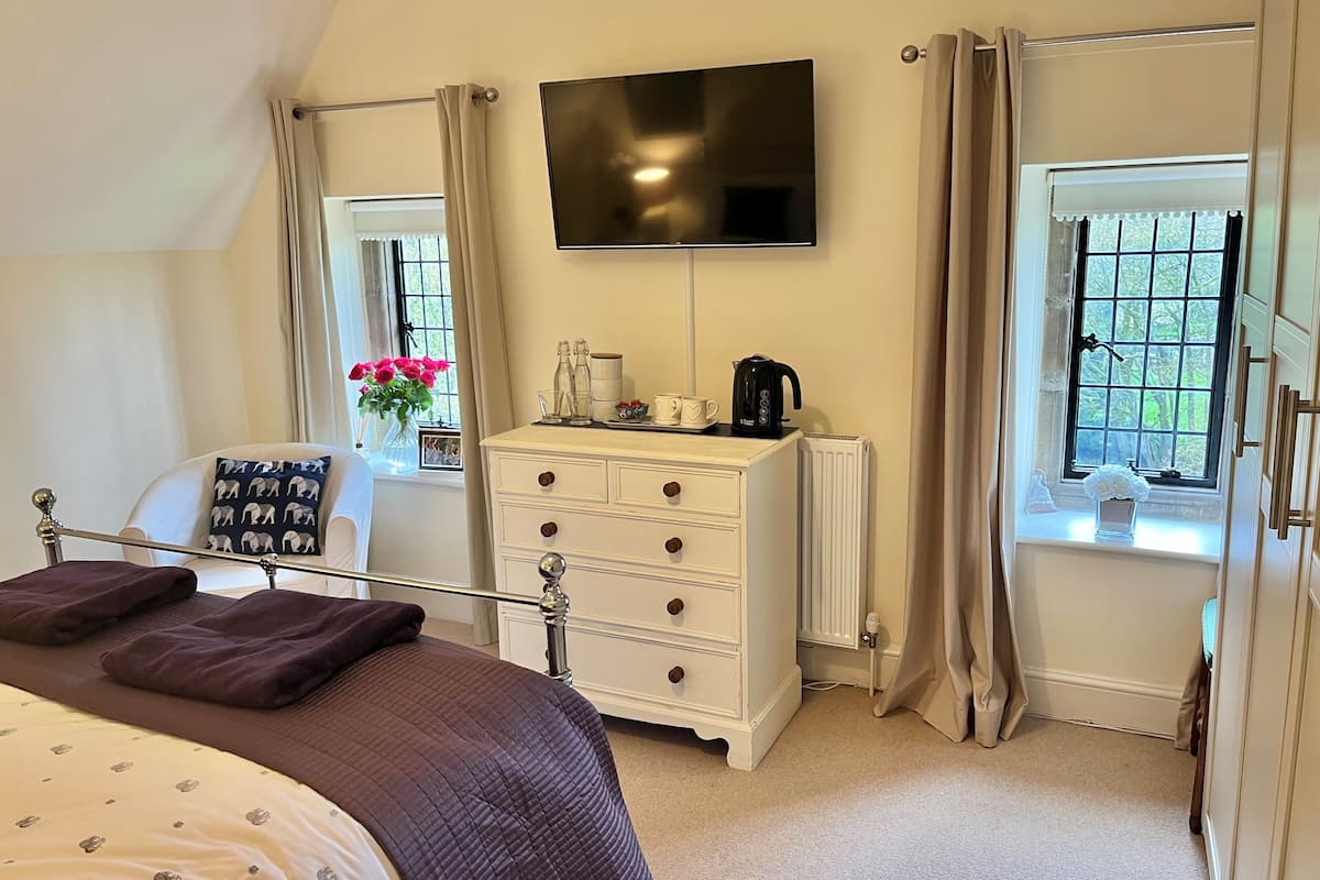 A bedroom with a bed, a dresser, a television, and two windows with curtains.