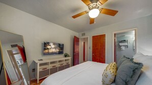 Une chambre à coucher avec un lit, un ventilateur de plafond, un téléviseur fixé au mur, une armoire et un miroir.