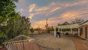 Un espace extérieur abrité comprenant un hamac, une terrasse avec des chaises et une pergola.