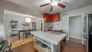 Une cuisine moderne avec un plancher en bois, un îlot central, un ventilateur de plafond et un réfrigérateur.