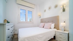 Une chambre à coucher comprenant un lit, une commode, une table de chevet, une fenêtre et des appliques murales.