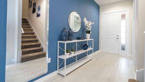 Un pasillo moderno con una pared azul de acento, una consola blanca con adornos, un espejo y una puerta blanca.