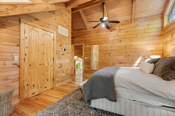 Ein Schlafzimmer einer Holzhütte mit einem Bett, einem Deckenventilator und einem Fenster.