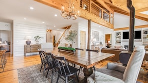Amplia sala de estar con un gran comedor de madera, asientos cómodos, una escalera que sube a un nivel superior y una acogedora chimenea.