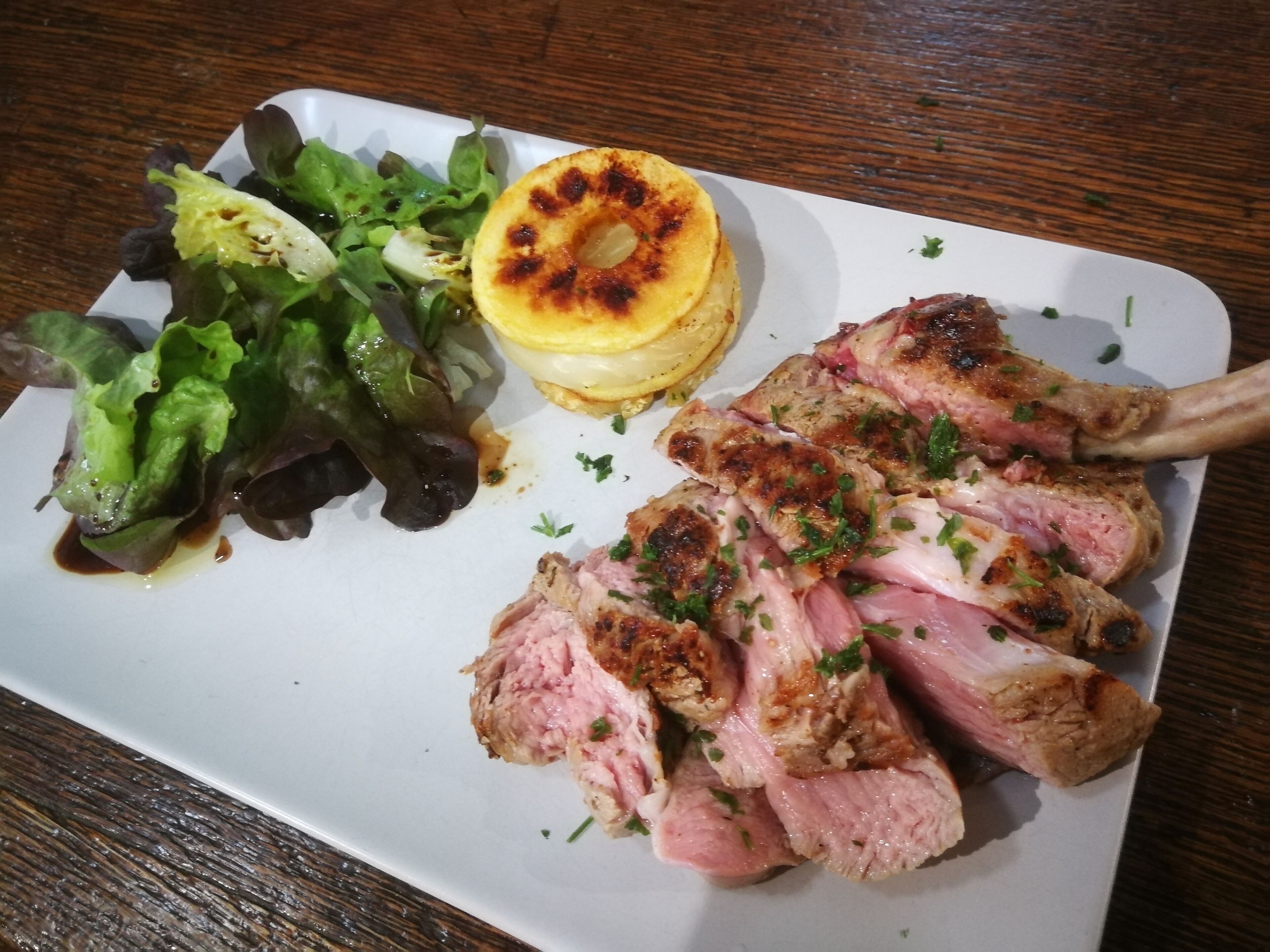 Une assiette avec des tranches de viande, une pomme de terre grillée et une salade en accompagnement.