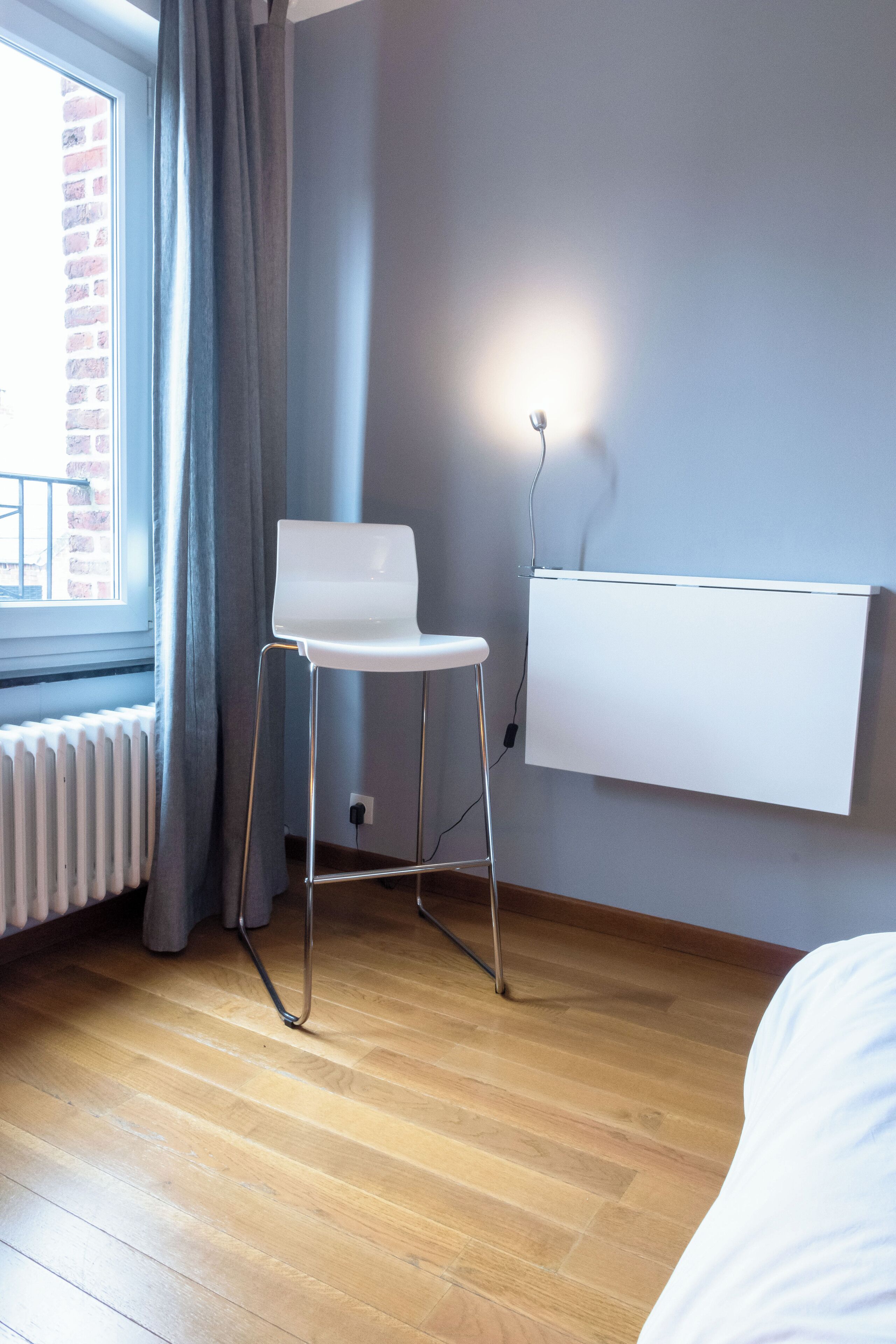 A room with a wooden floor, a white chair, a whiteboard on the wall, and a window with curtains.
