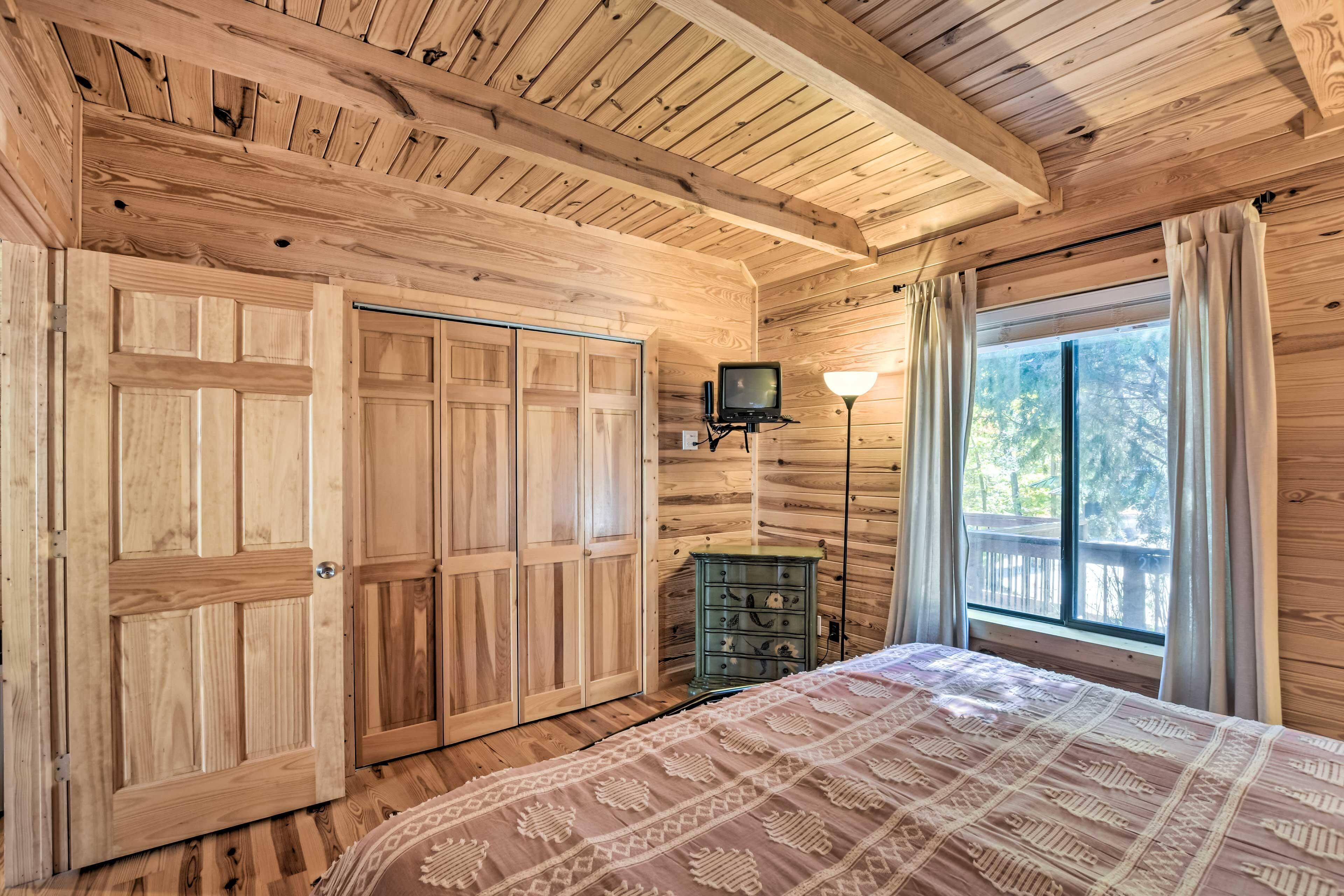 Un dormitorio con paneles de madera, una cama, un tocador, un televisor y una ventana con cortinas.