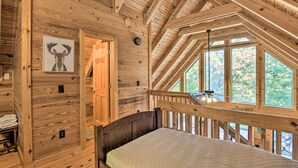 Ein Schlafzimmer einer Holzhütte mit Bett, Deckenventilator und großen Fenstern mit Blick ins Freie.