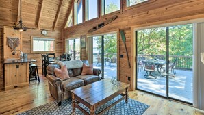 Ein geräumiges Blockhaus-Interieur mit Holzbalkendecke, großen Fenstern, einer gemütlichen Sitzecke und einer Terrasse.