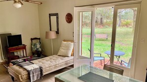A small, cozy room with a bed, a TV, a lamp, and a table by a sliding glass door leading to a garden.