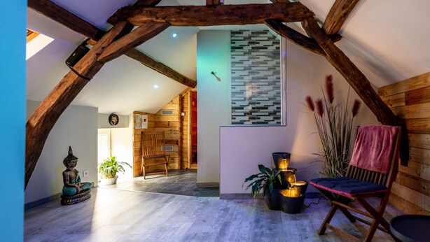 Un intérieur rustique avec des poutres apparentes, une statue de méditation, un banc et un luminaire fixé au mur.