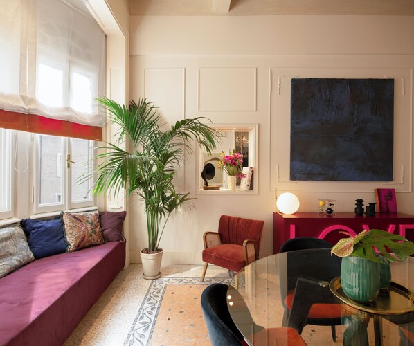 A cozy living room with a sofa, a dining table, a potted plant, and a large abstract painting on the wall.